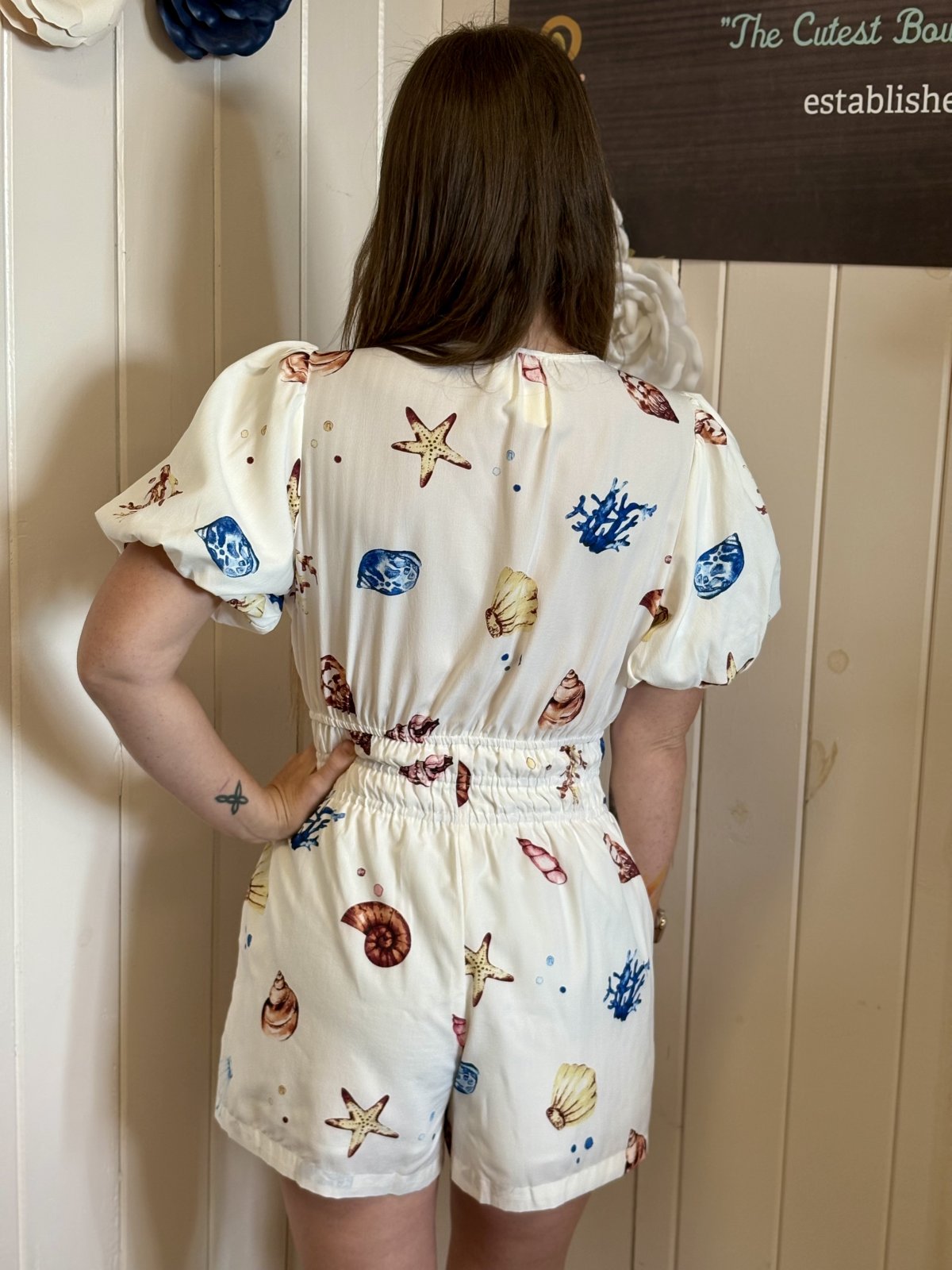 Back view of Off-White Shell Print Romper with puff sleeves, perfect for coastal boutique clothing and tropical vacations.