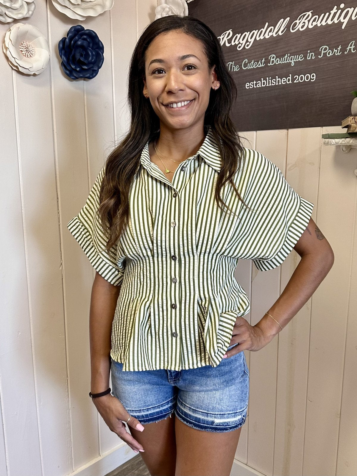 Kendra Top model wearing a cream button-down with olive stripes at Raggdoll Boutique in Port Aransas, showcasing trendy coastal style.