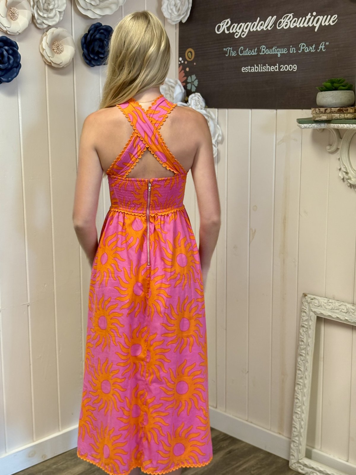 Back view of a vibrant pink and orange sun-patterned dress, perfect for summer events from a coastal boutique.