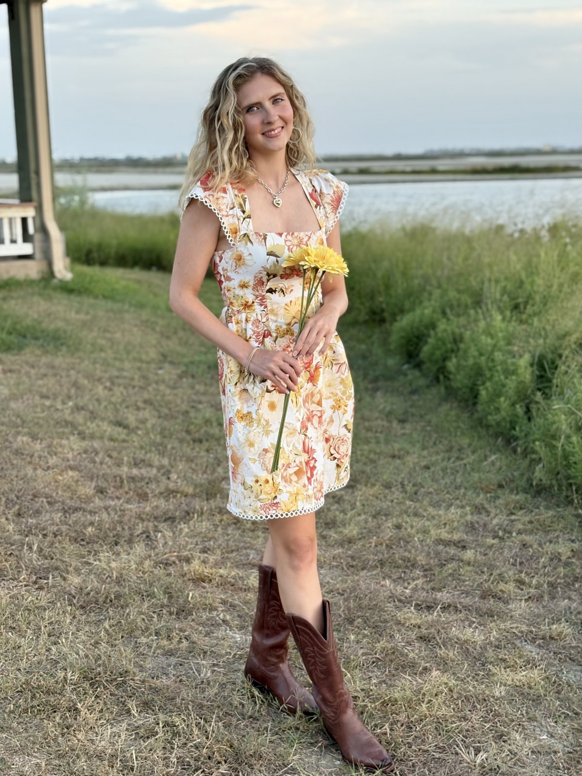 Model in floral mini dress with cowboy boots, showcasing autumn charm from a Port Aransas boutique for coastal fashion.