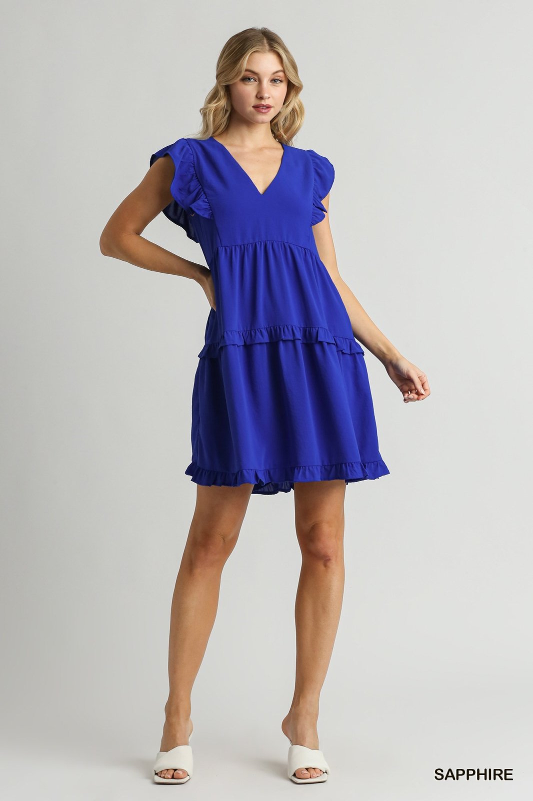 Sapphire blue ruffle tiered dress with V-neck, perfect for coastal boutiques and tropical vacations, stylish and functional.
