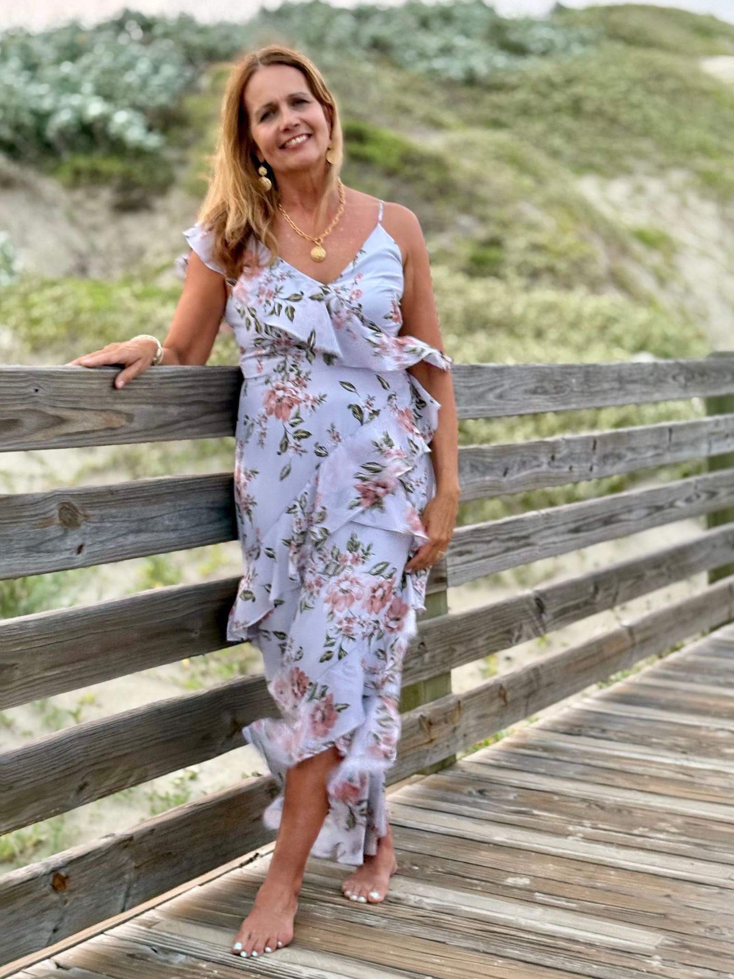 Woman in floral beach dress on wooden path, showcasing coastal boutique clothing and curated women's fashion.