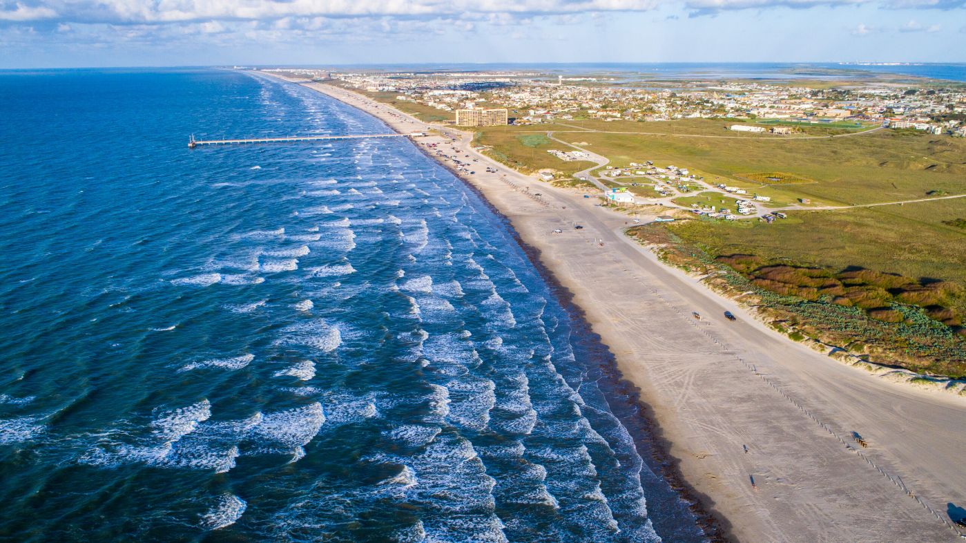 Aerial view of a sandy beach and coastline in Port Aransas, showcasing waves and the Texas coastal landscape.