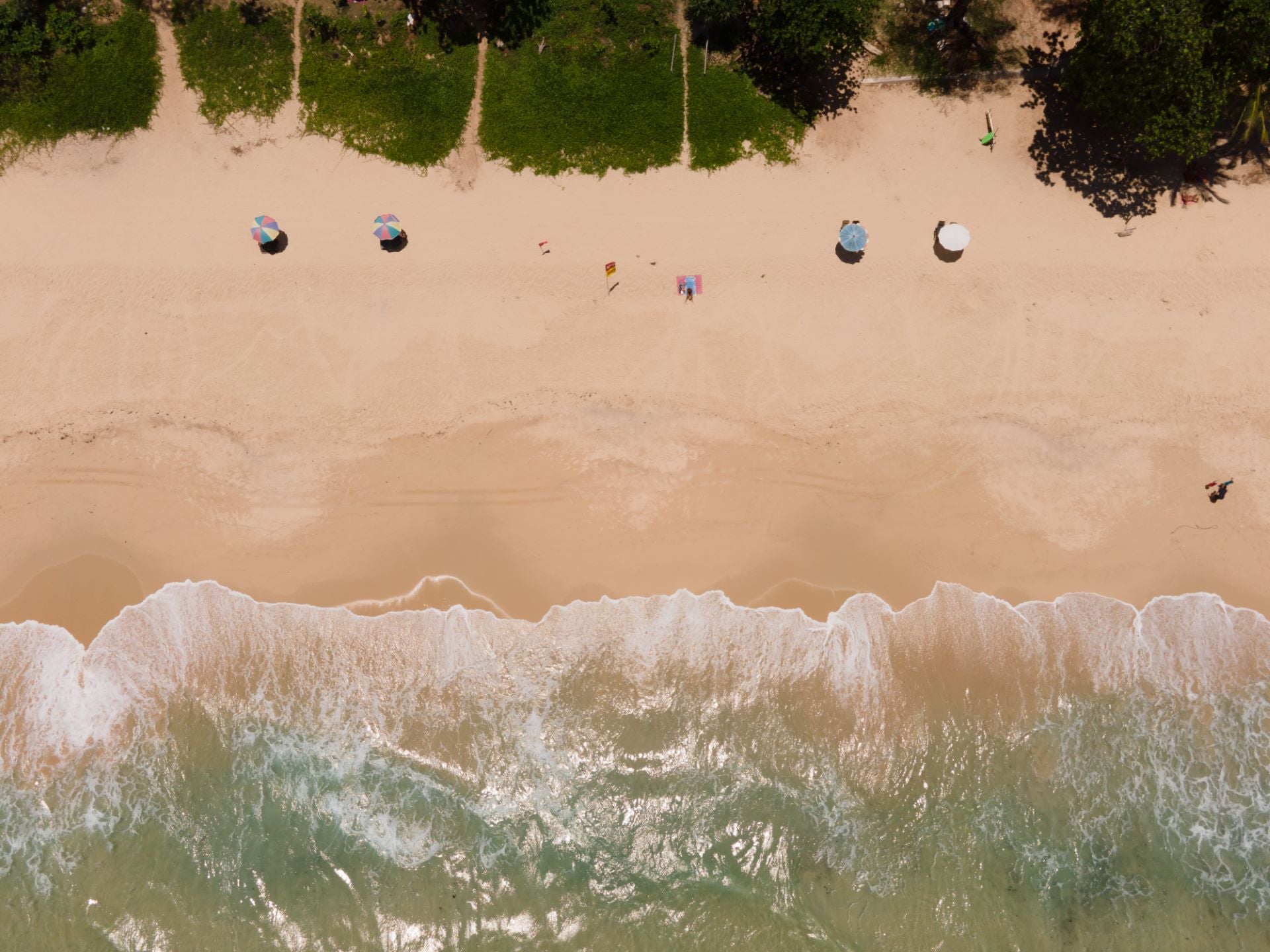 Aerial view of a sandy beach with umbrellas, perfect for showcasing coastal boutique clothing and tropical vacation dresses.