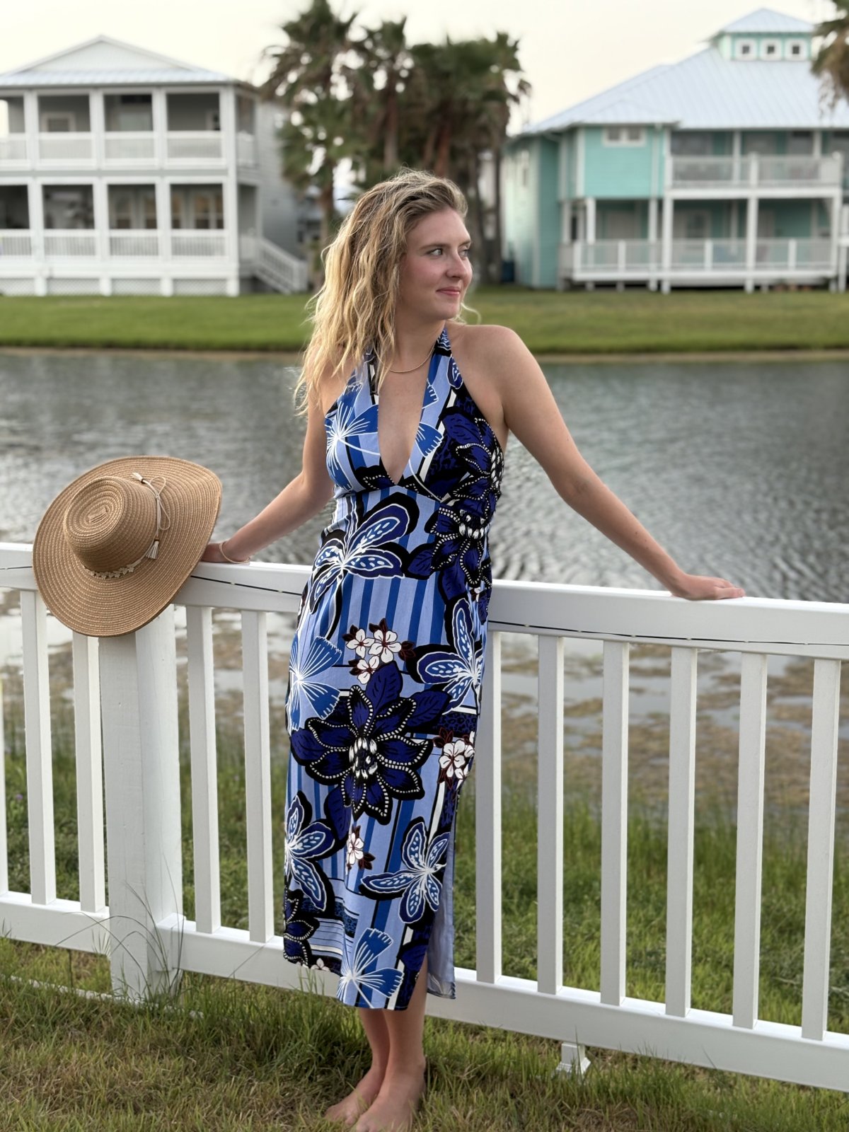 Woman in blue multi halter-style dress by the water, perfect for tropical vacations and coastal boutique clothing.