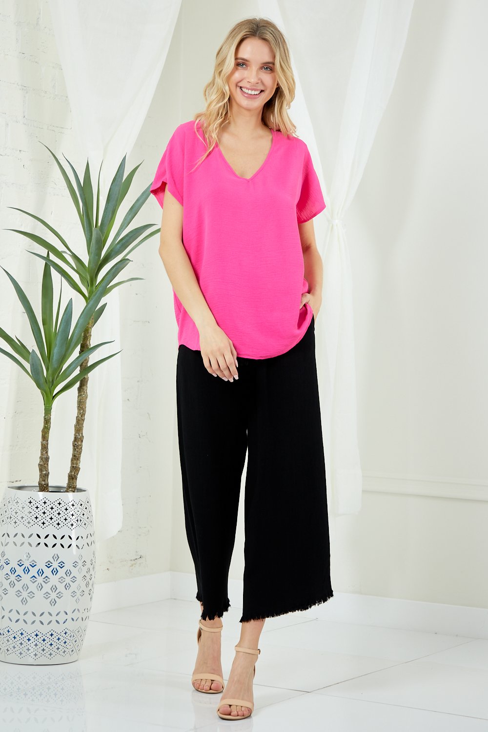 Model wearing HOT PINK V-NECK SOLID SIMPLE TOP with black pants at Raggdoll Boutique, showcasing trendy coastal style.