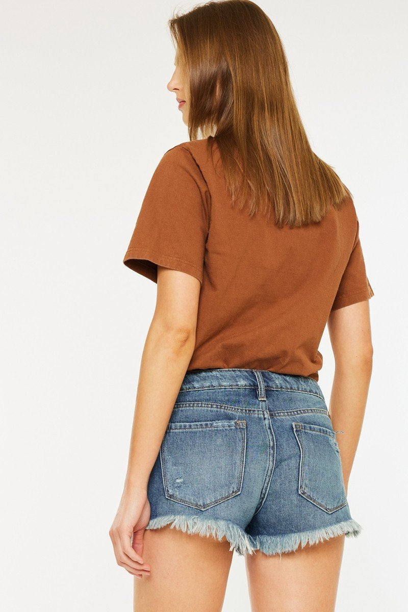 Back view of model wearing Kancan mid-rise jean shorts and a brown tee, showcasing stylish women's bottoms for summer outings.