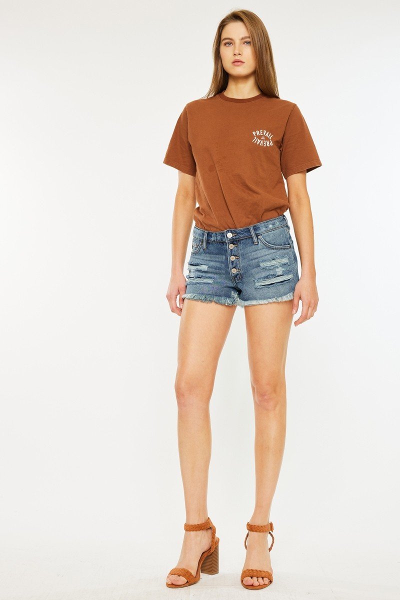 Stylish model wearing Kancan mid-rise jean shorts and brown graphic tee, perfect for summer beach outings and casual fashion.