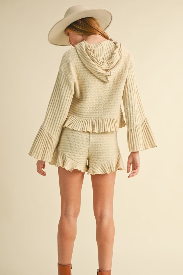 Chic coastal boutique clothing featuring a hooded long sleeve top with ruffle shorts, perfect for tropical vacations.