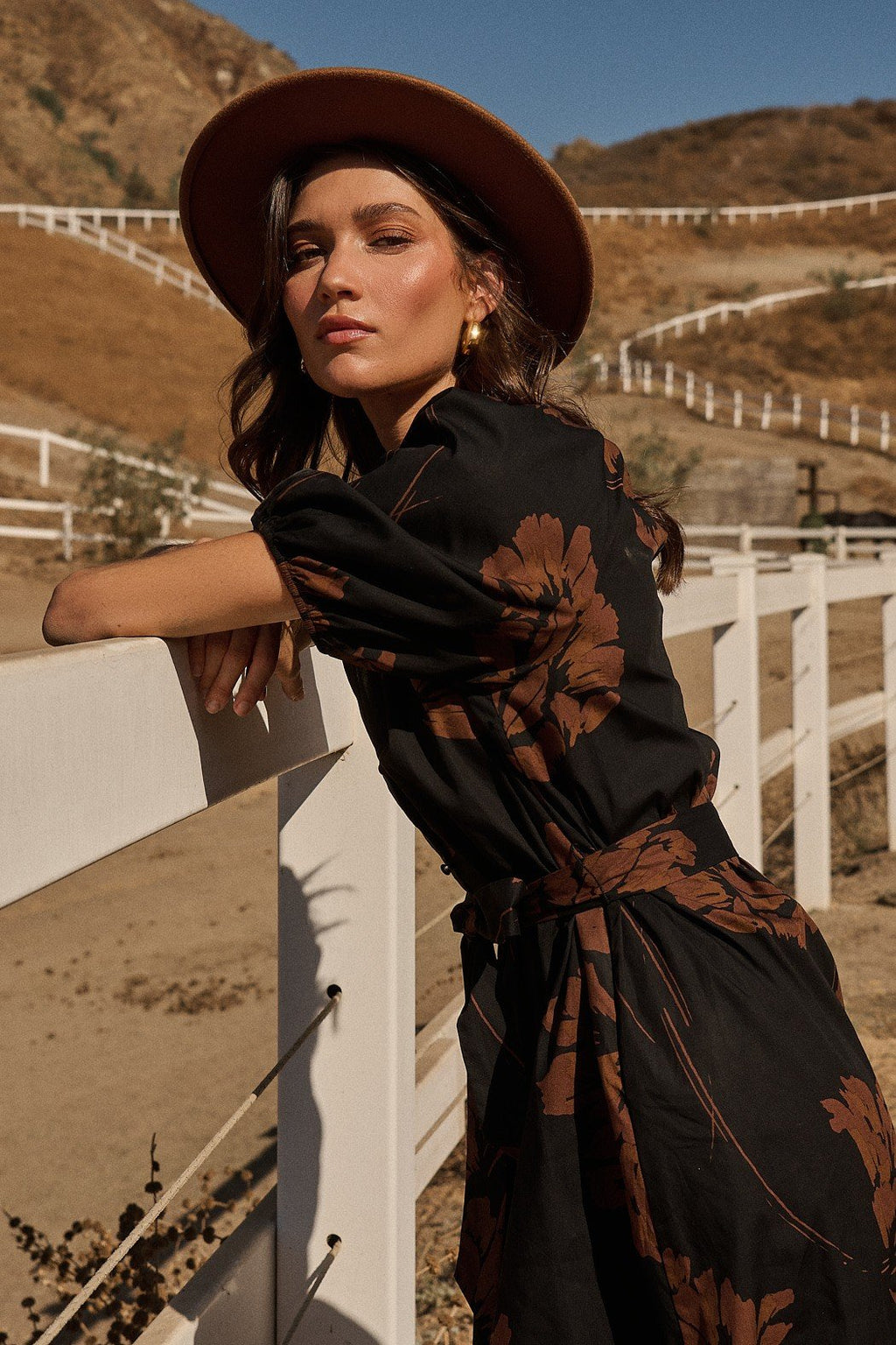 Model wearing Celina Floral Wynette Tiered Midi Dress with puff sleeves and hat in sunny outdoor setting, perfect for coastal boutique clothing.