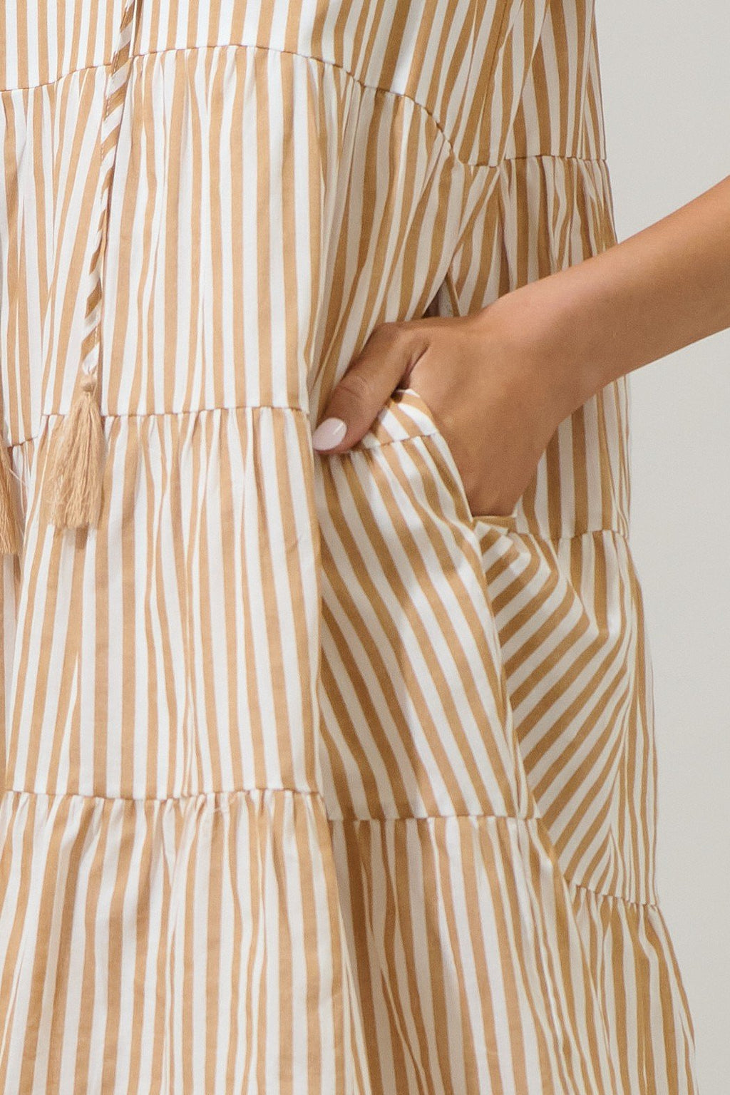Close-up of a taupe striped mini dress with ruffle sleeves, featuring a tassel tie and deep pockets. Perfect for summer outings.