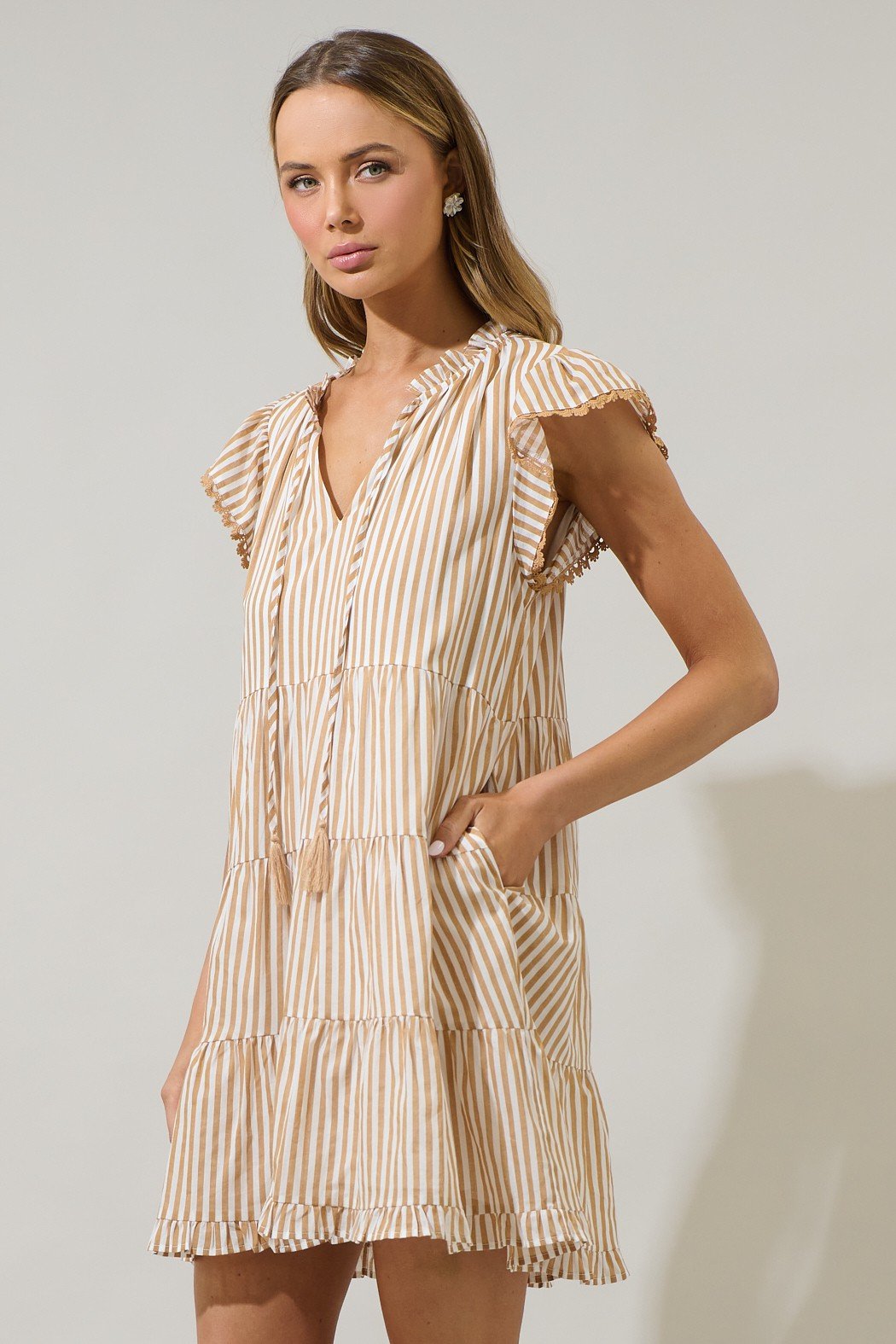 Stylish taupe striped mini dress with ruffle sleeves and tassel tie, perfect for summer from a coastal boutique.