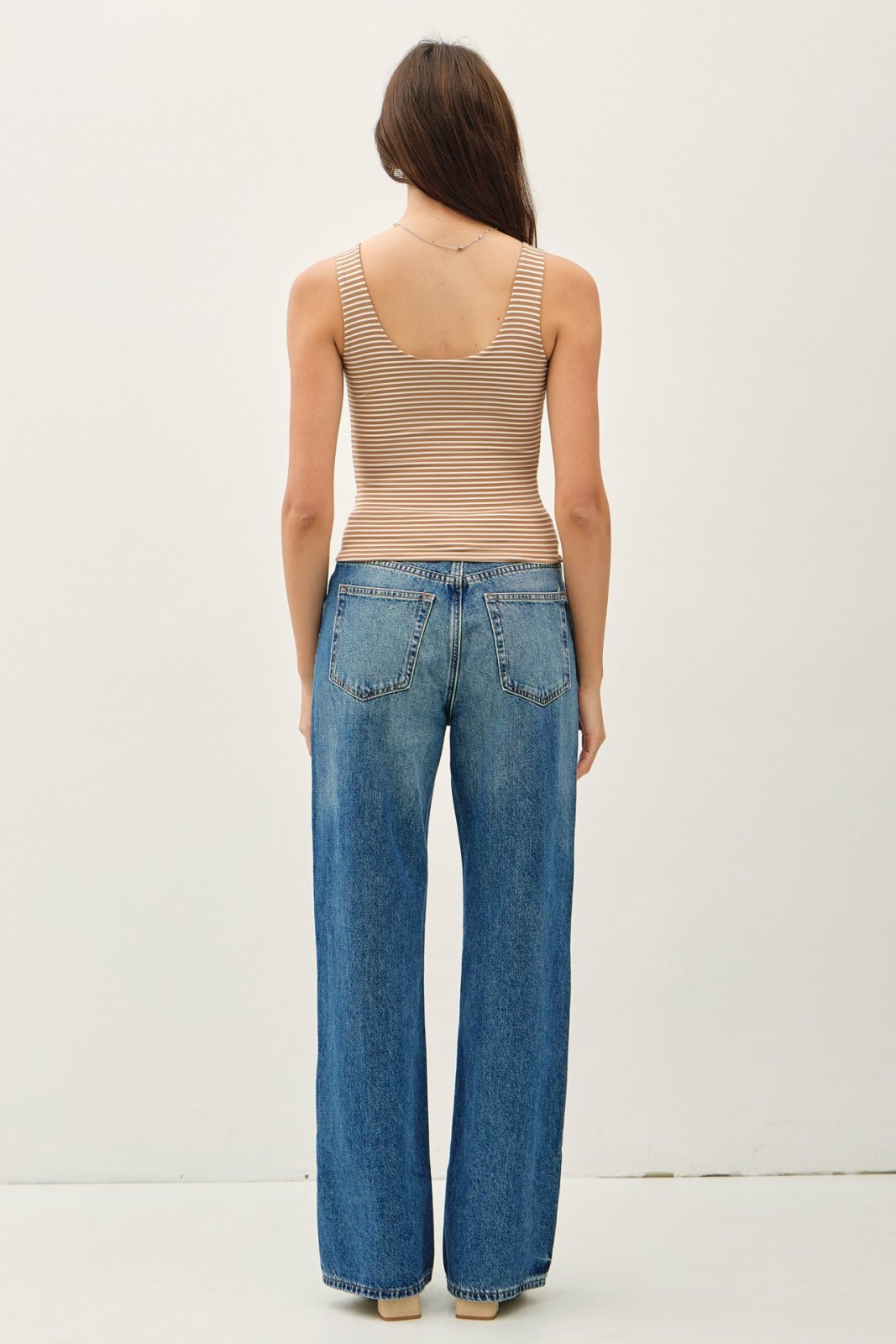 Back view of a model in a mocha stripe tank top and wide-leg jeans, showcasing coastal boutique clothing style.