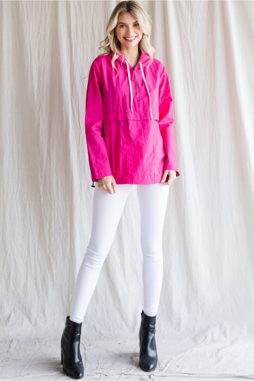 Vibrant pink windbreaker pullover from a coastal boutique, styled with white pants and black boots, perfect for beach outings.
