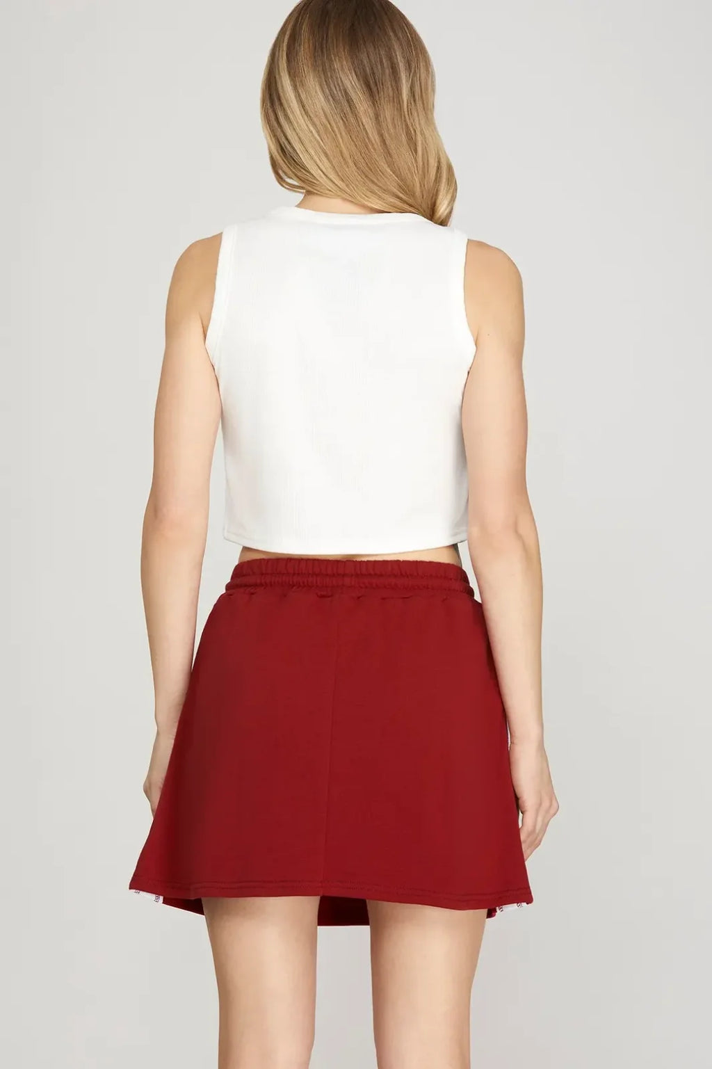 Back view of a woman wearing a high-waisted maroon mini skirt, showcasing coastal boutique clothing and stylish women's bottoms.