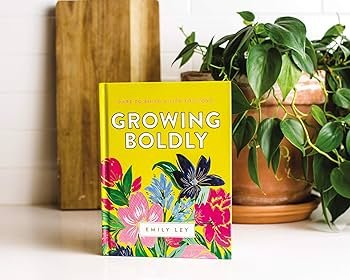 Book cover of GROWING BOLDLY by Emily Ley on a kitchen counter with green plants.