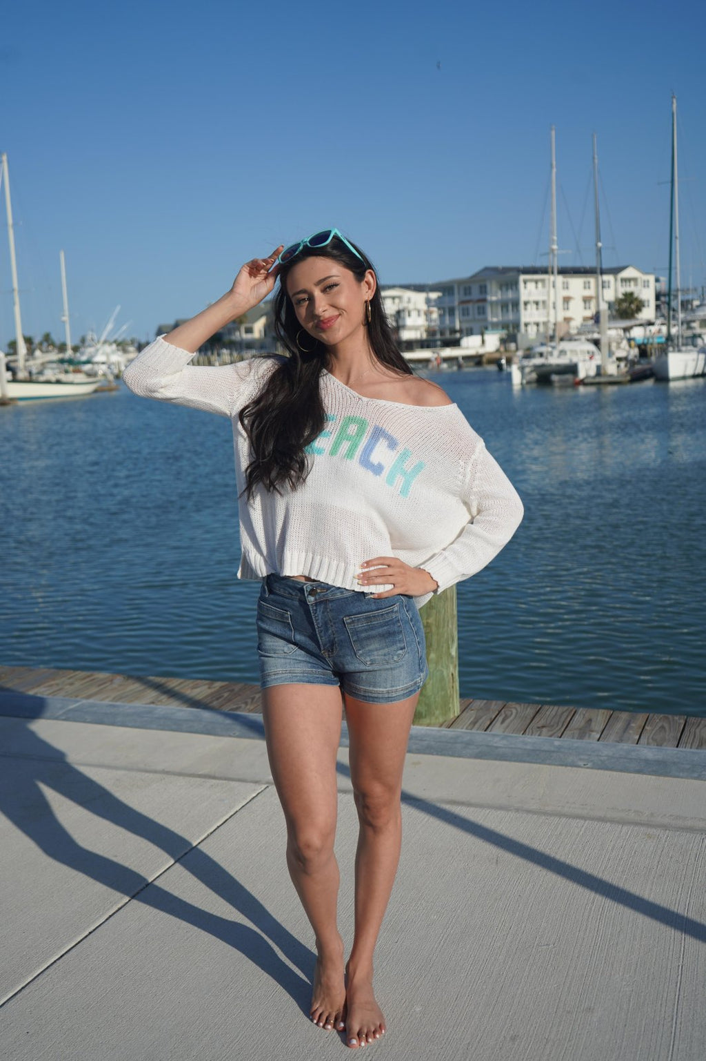 Woman wearing a slouchy beach sweater at a marina, perfect for coastal boutique clothing and summer outfits.