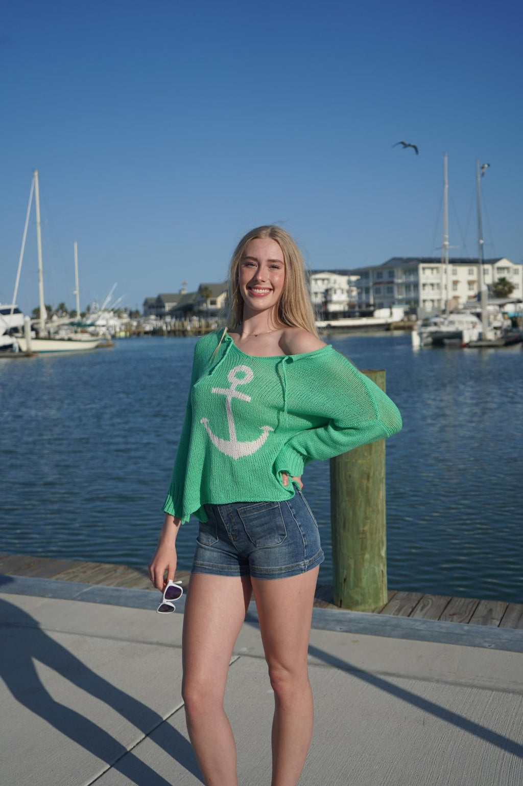 Model wearing a green Wooden Ships Anchor Sweater by the marina, perfect for coastal boutique clothing and beach vibes.