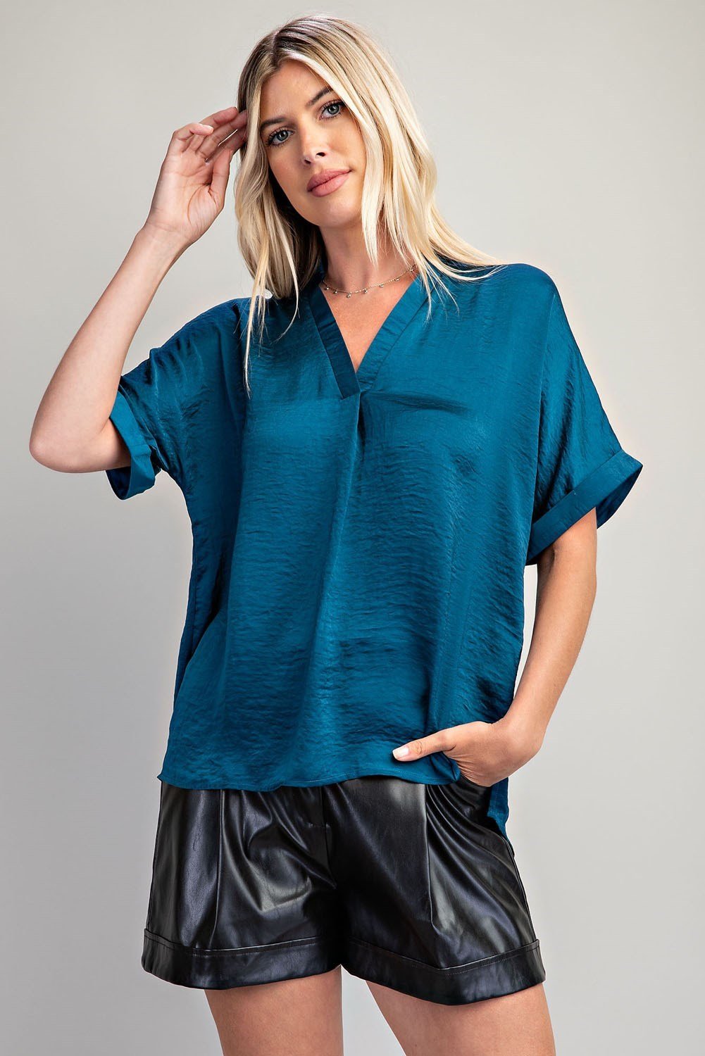 Stylish teal top in a coastal boutique, perfect for tropical vacations and paired with leather shorts for curated women's fashion.
