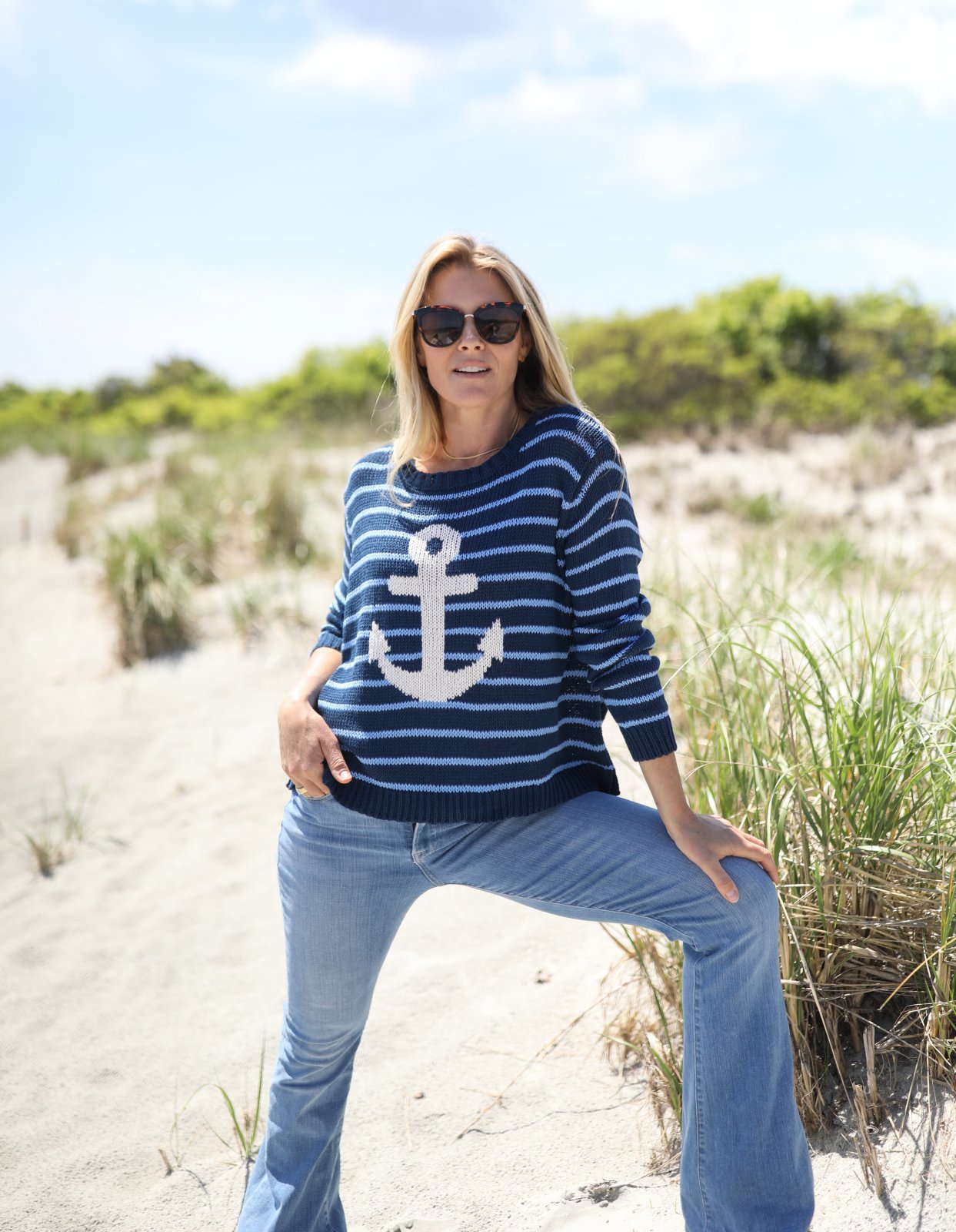 Woman wearing WS Wooden Ships anchor striped crew sweater at the beach, showcasing coastal boutique clothing style.