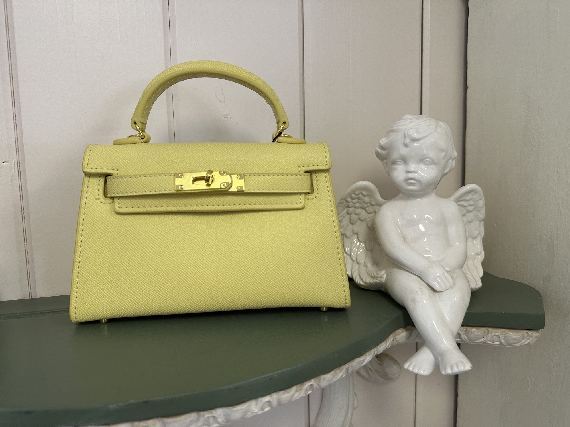 Stylish yellow Jackie Bag displayed beside a cute angel statue, perfect for beach dresses and tropical vacation outfits.