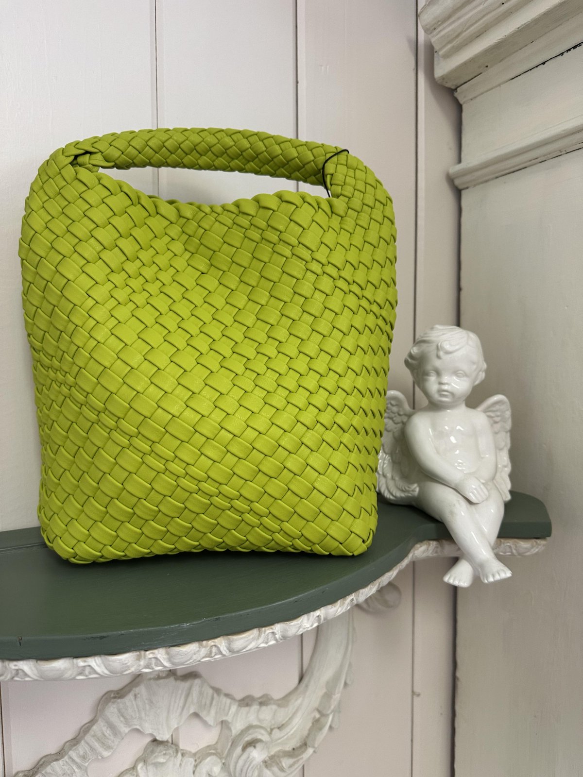 Stylish green woven mini tote bag next to a decorative angel, perfect for coastal boutique clothing and spring outings.