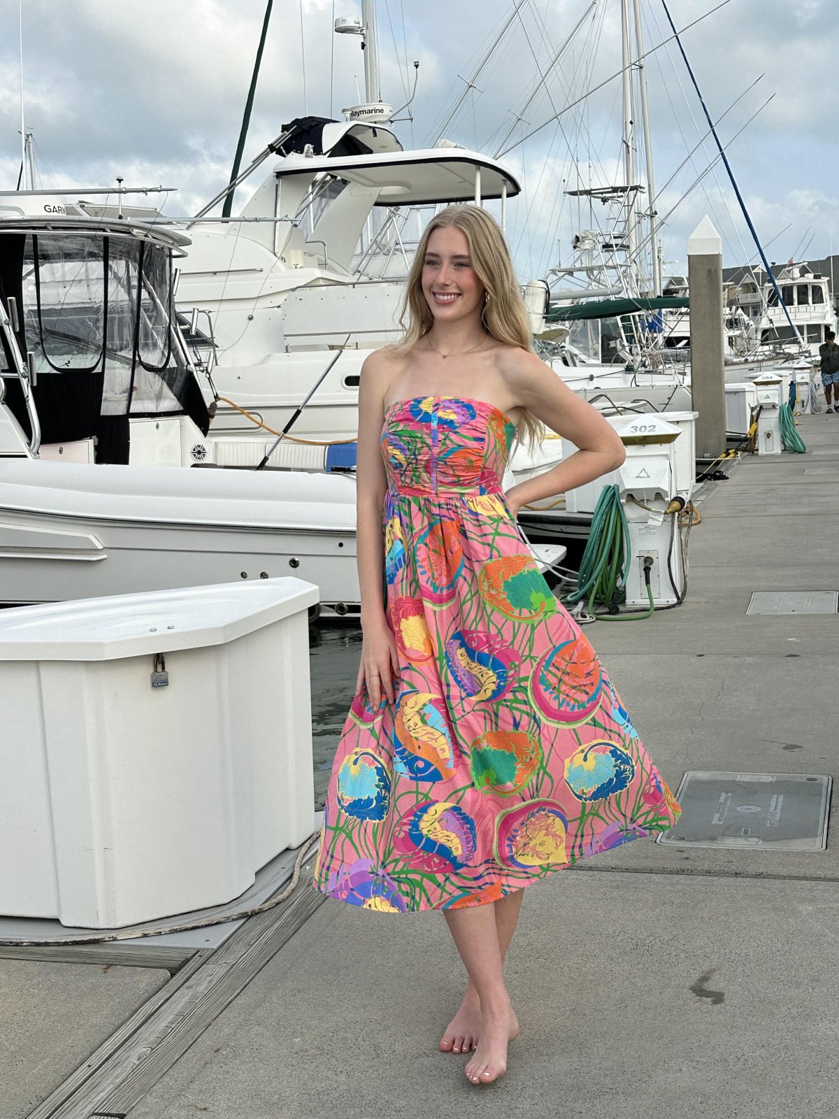 Model wearing a colorful strapless dress by a marina, perfect for coastal boutique clothing and tropical vacations.