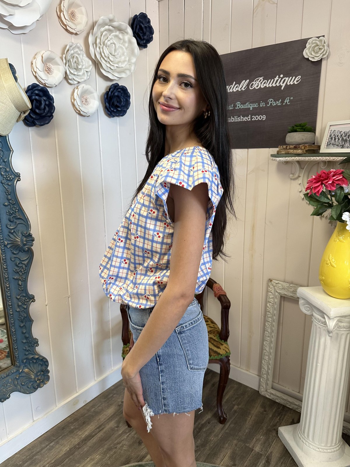 Charming cherry print blouse showcased in a boutique; perfect for casual outings and women's fashion. Coastal boutique clothing.