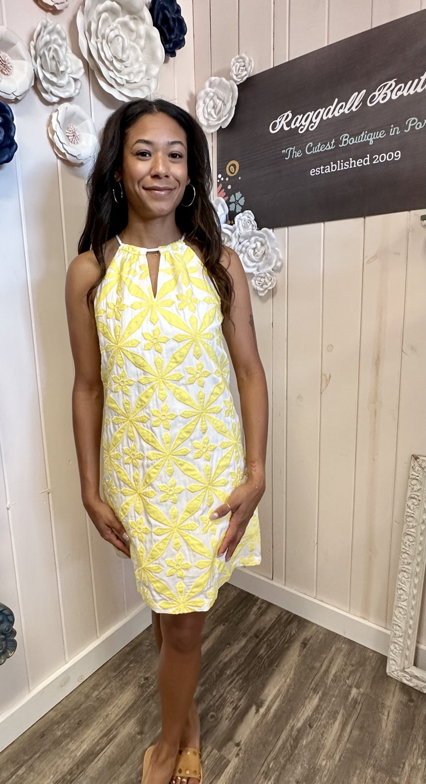 A woman wearing a bright yellow halter dress with intricate embroidery, showcasing coastal boutique clothing for summer events.