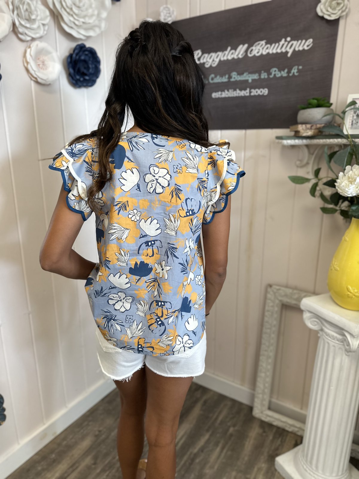 Coastal boutique clothing: Slate Blue Floral Print Flutter Sleeve Top styled with white shorts, perfect for tropical vacations.