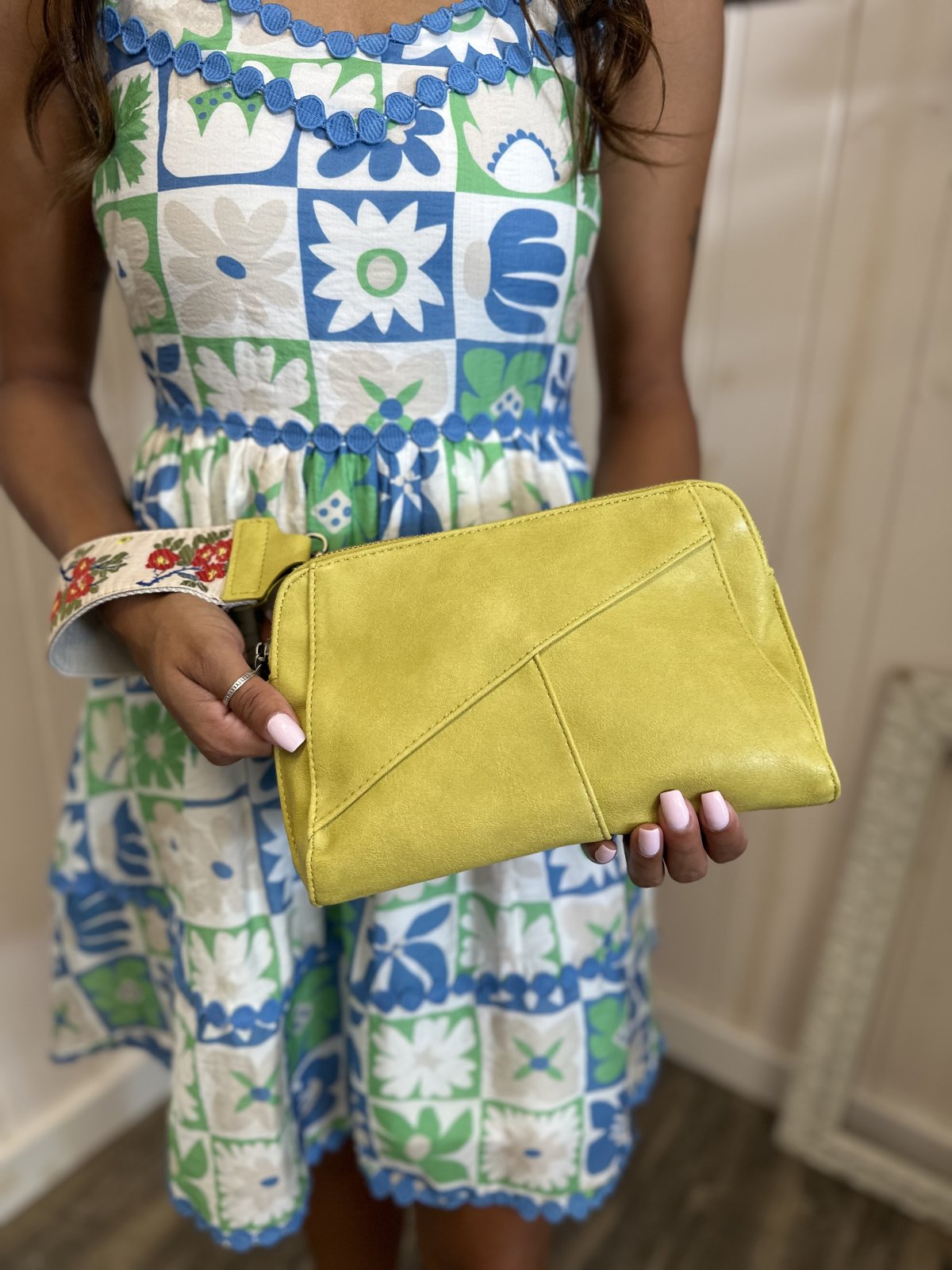 Woman holding a vibrant yellow clutch, wearing a floral print dress, perfect for beach outings and coastal boutique styling.