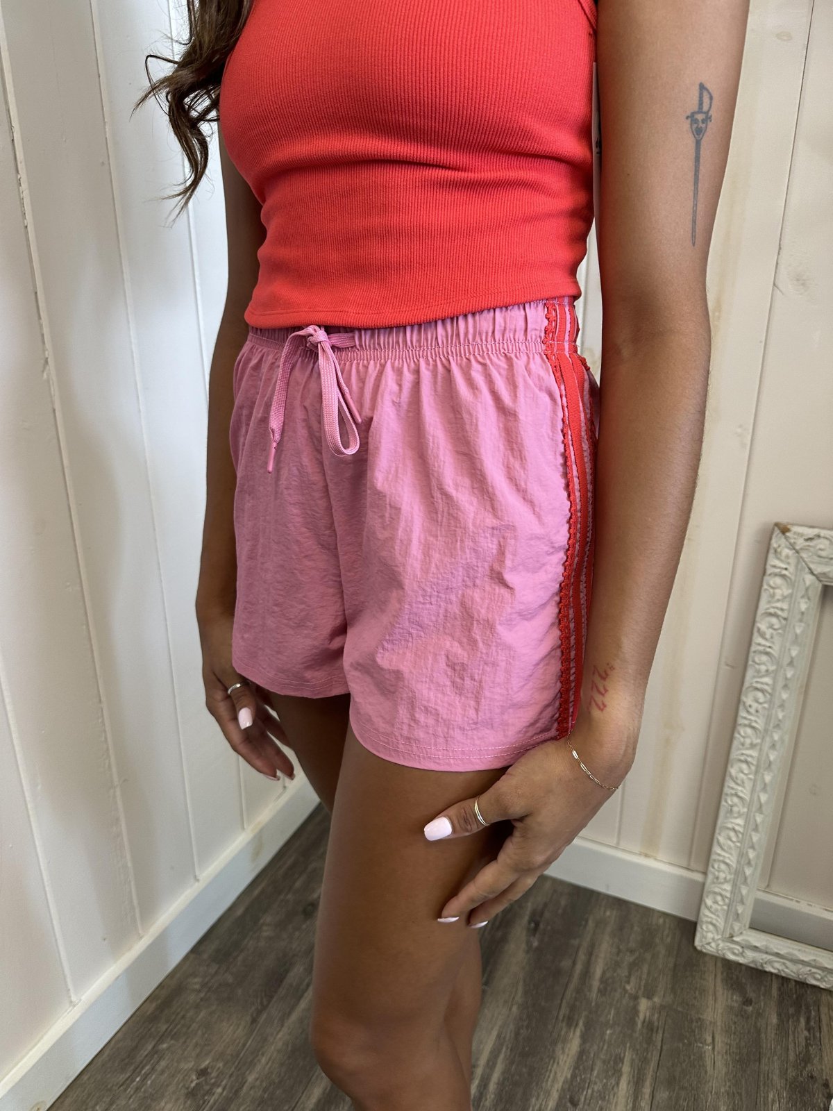 Stylish pink side stripe and lace trim shorts for women, perfect for beach outings or casual days at a coastal boutique.