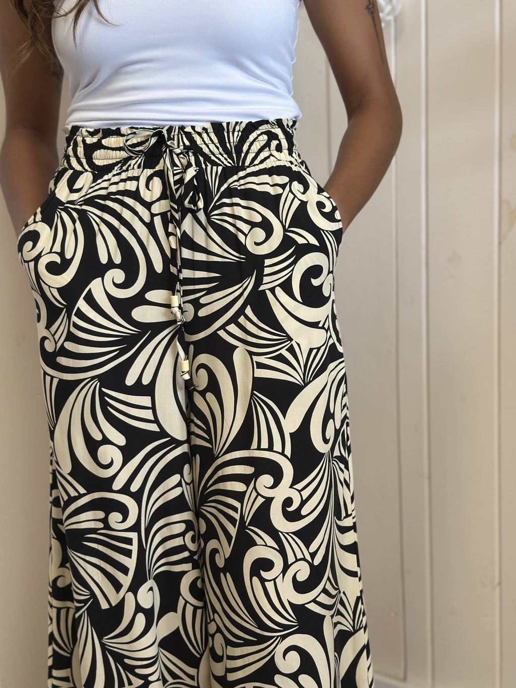Stylish black printed wide leg pants with pockets and ruffled waistband from a coastal boutique, perfect for women's fashion.