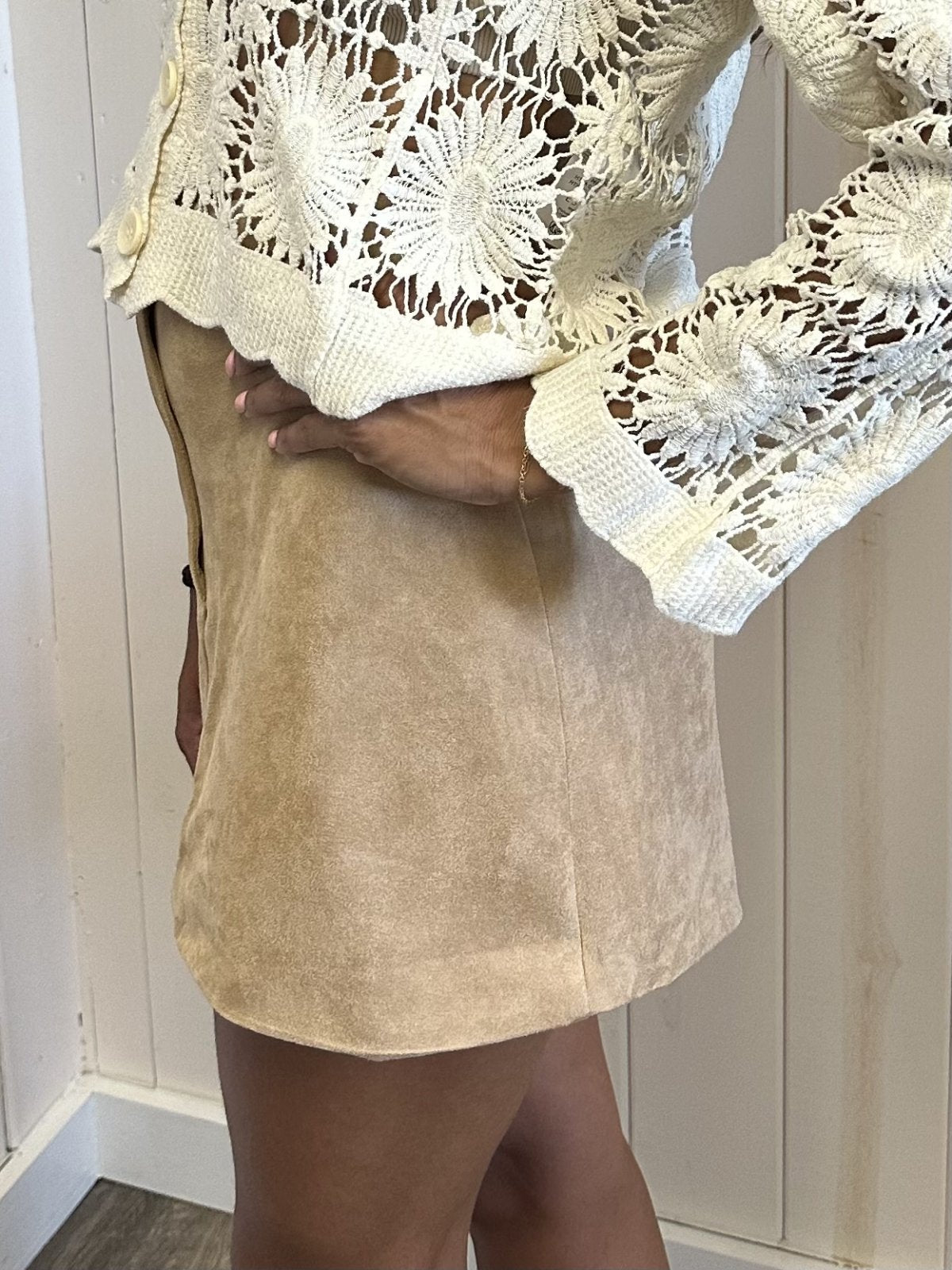 Woman wearing the Mae Skirt, a beige suede mini skirt, paired with a crocheted top for a trendy coastal style.