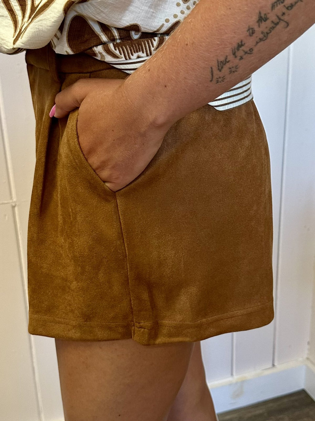 Model wearing Margot Shorts, showcasing high-waist design and side pockets in camel suede-like fabric, perfect for coastal fashion.