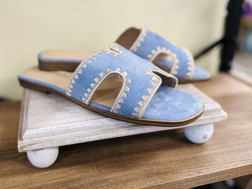 Stylish blue suede slide sandals with cut-out design and stitched edges, perfect for coastal boutique clothing and summer fashion.