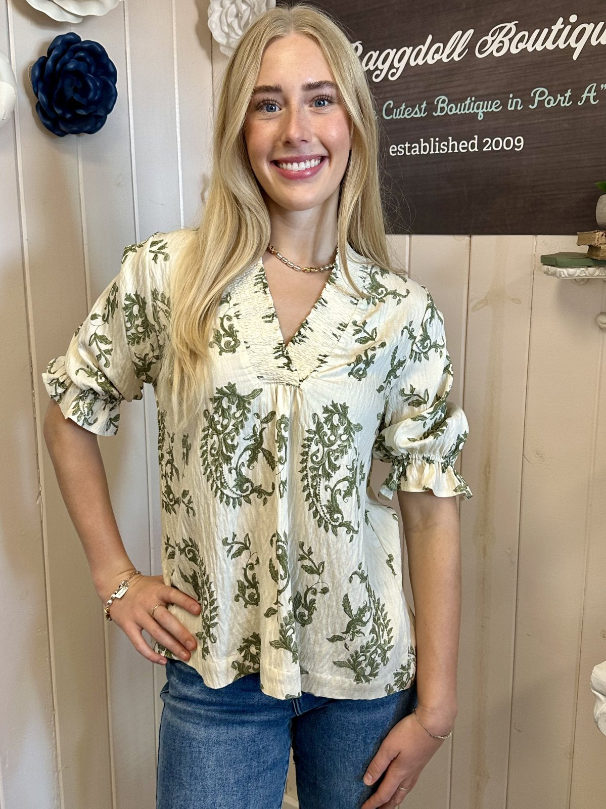 Smiling woman in floral blouse from Raggdoll Boutique, showcasing trendy coastal style & women's clothing in Port Aransas.