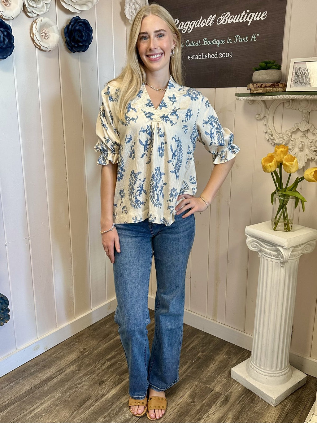 Woman in floral boutique top and flared jeans at Raggdoll Boutique, showcasing trendy coastal style in Port Aransas.