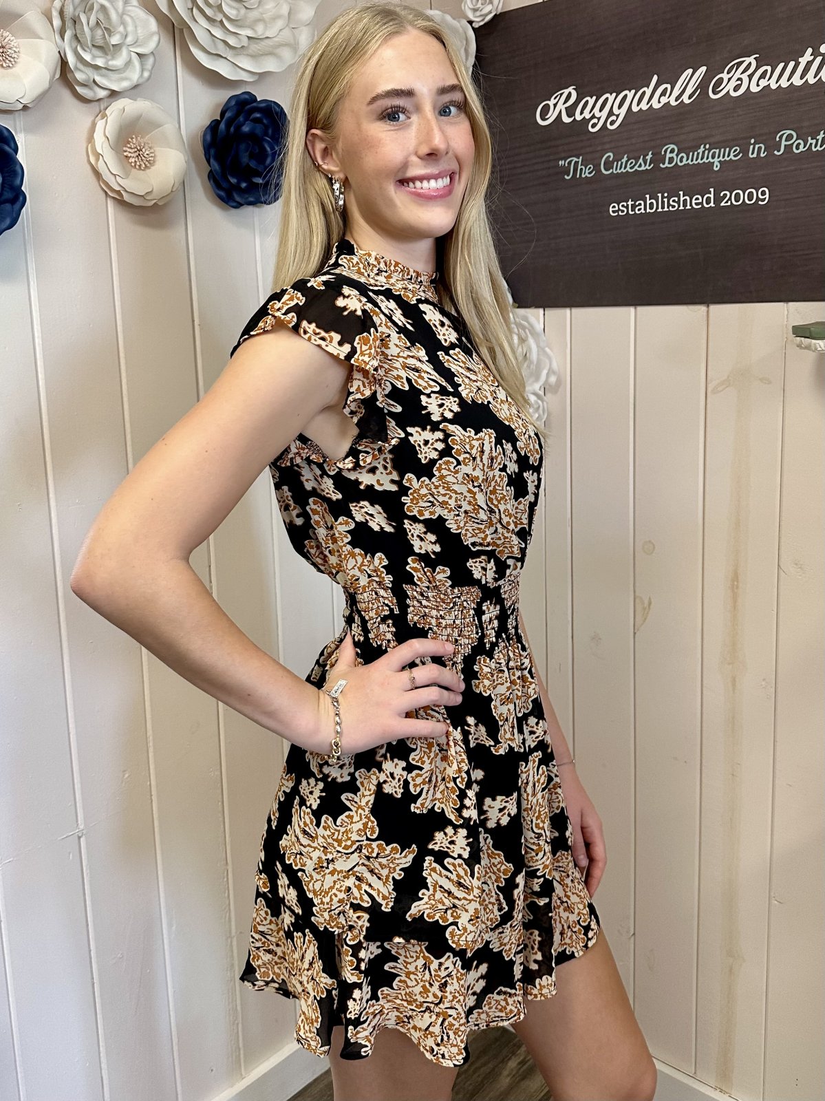 Barrett Dress showcased on a model at Raggdoll Boutique, featuring a black printed design and smocked waist detail.