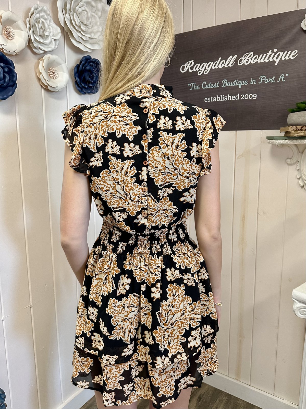 Back view of a woman wearing the Barrett Dress from Raggdoll Boutique, featuring a smocked waist and floral print.