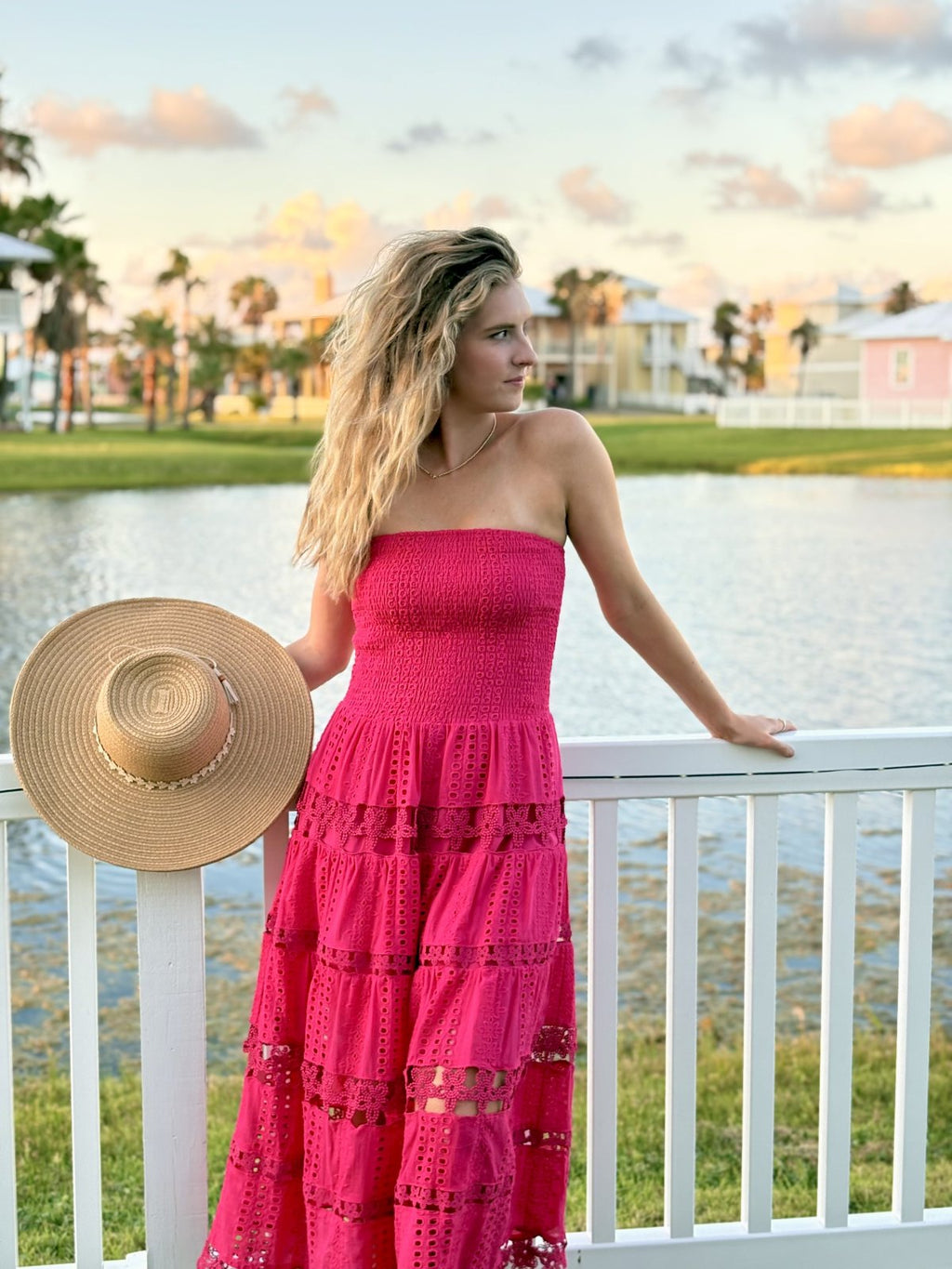 Nixie Dress in fuchsia worn by a woman with a straw hat near a waterfront, perfect for summer parties and vacations.
