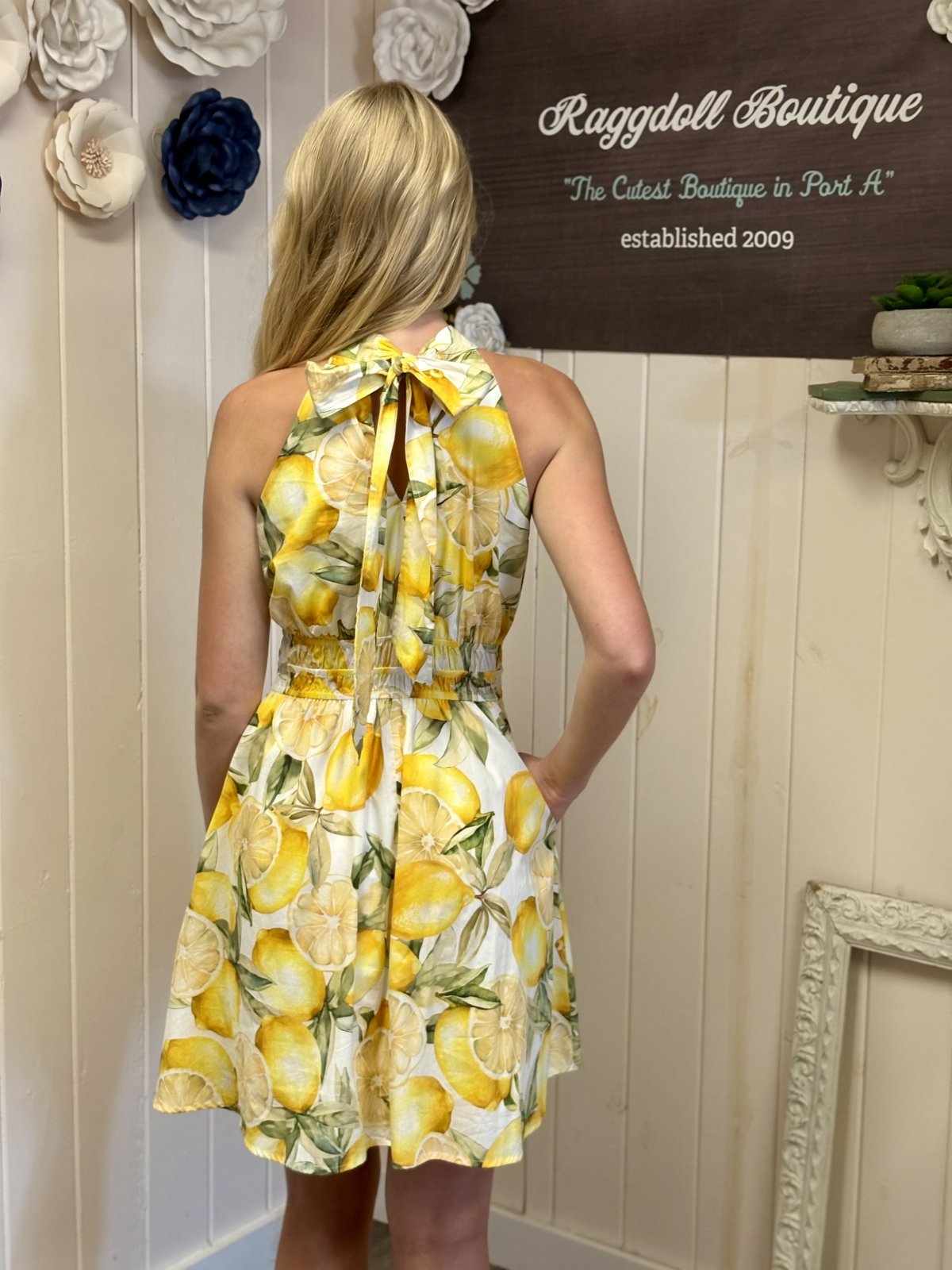 Back view of a white lemon print mini dress from a coastal boutique, perfect for summer beachwear.