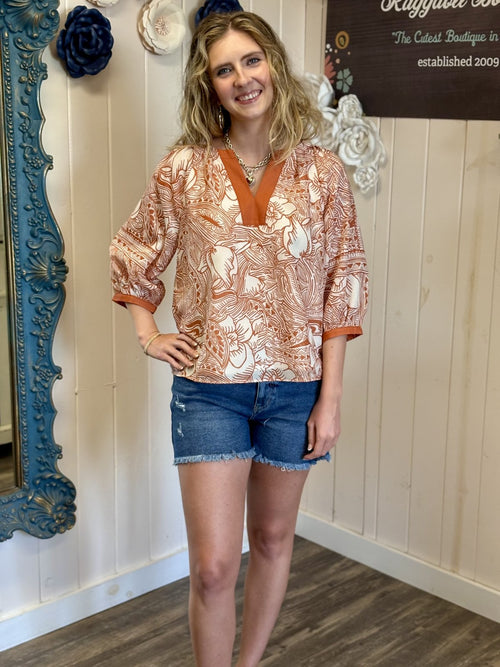 Styled model wearing a floral orange and white top with shorts in a coastal boutique, showcasing curated women's fashion.