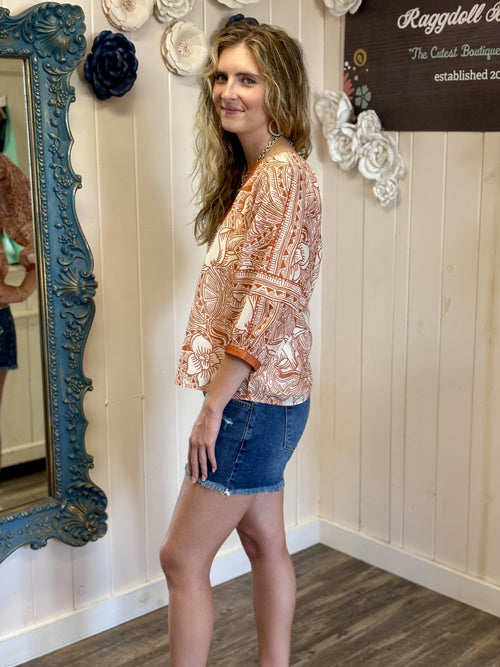 Orange and white top with 3/4 sleeves presented in a coastal boutique, perfect for stylish game day outfits.