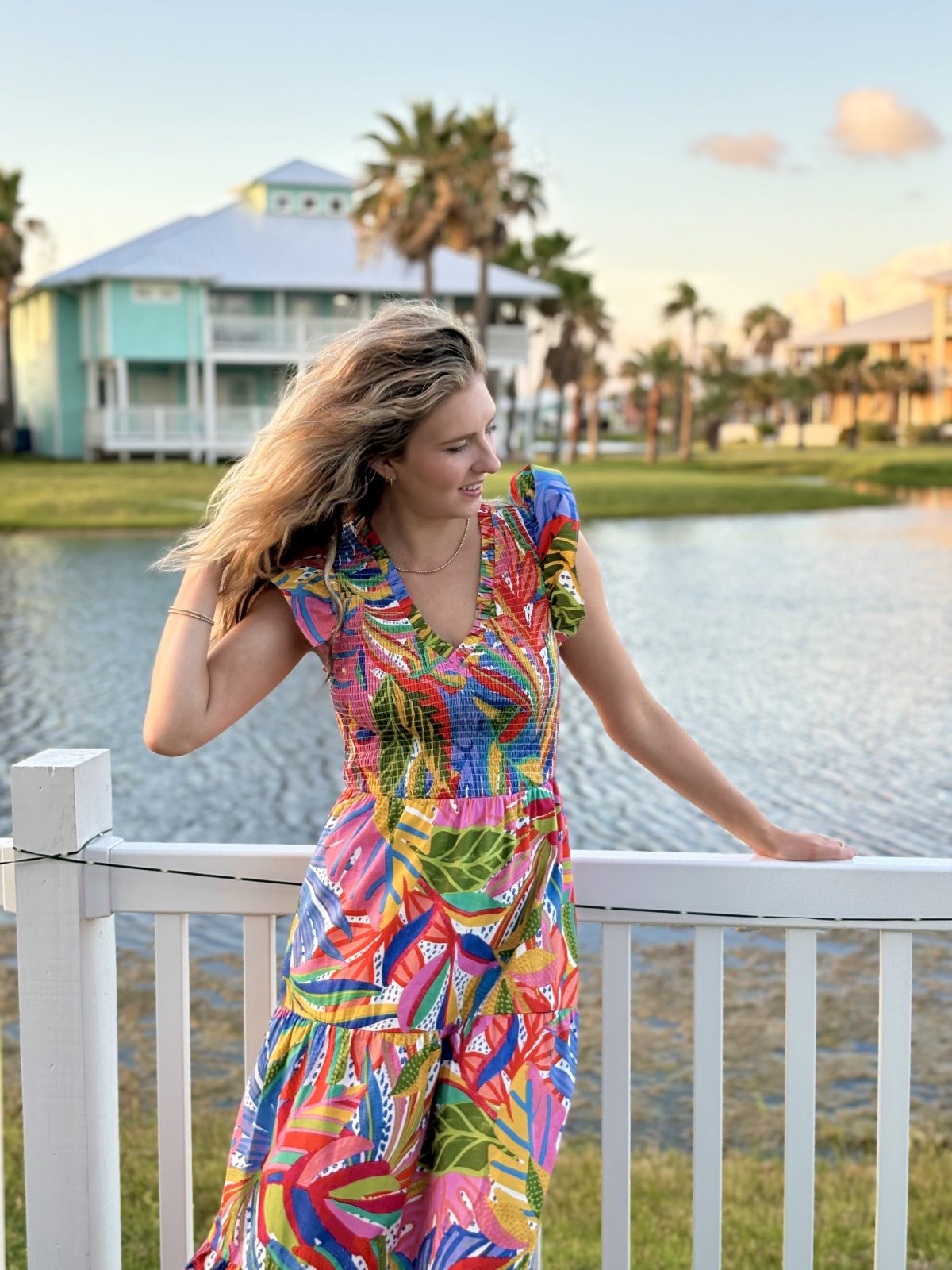 Woman wearing a colorful floral Giselle dress by the water, perfect for coastal boutique clothing and beach dresses.