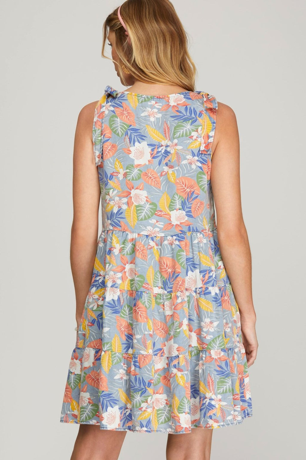 Back view of a woman wearing the SUMMER VIBES DRESS from Raggdoll Boutique, showcasing vibrant floral pattern and trendy coastal style.