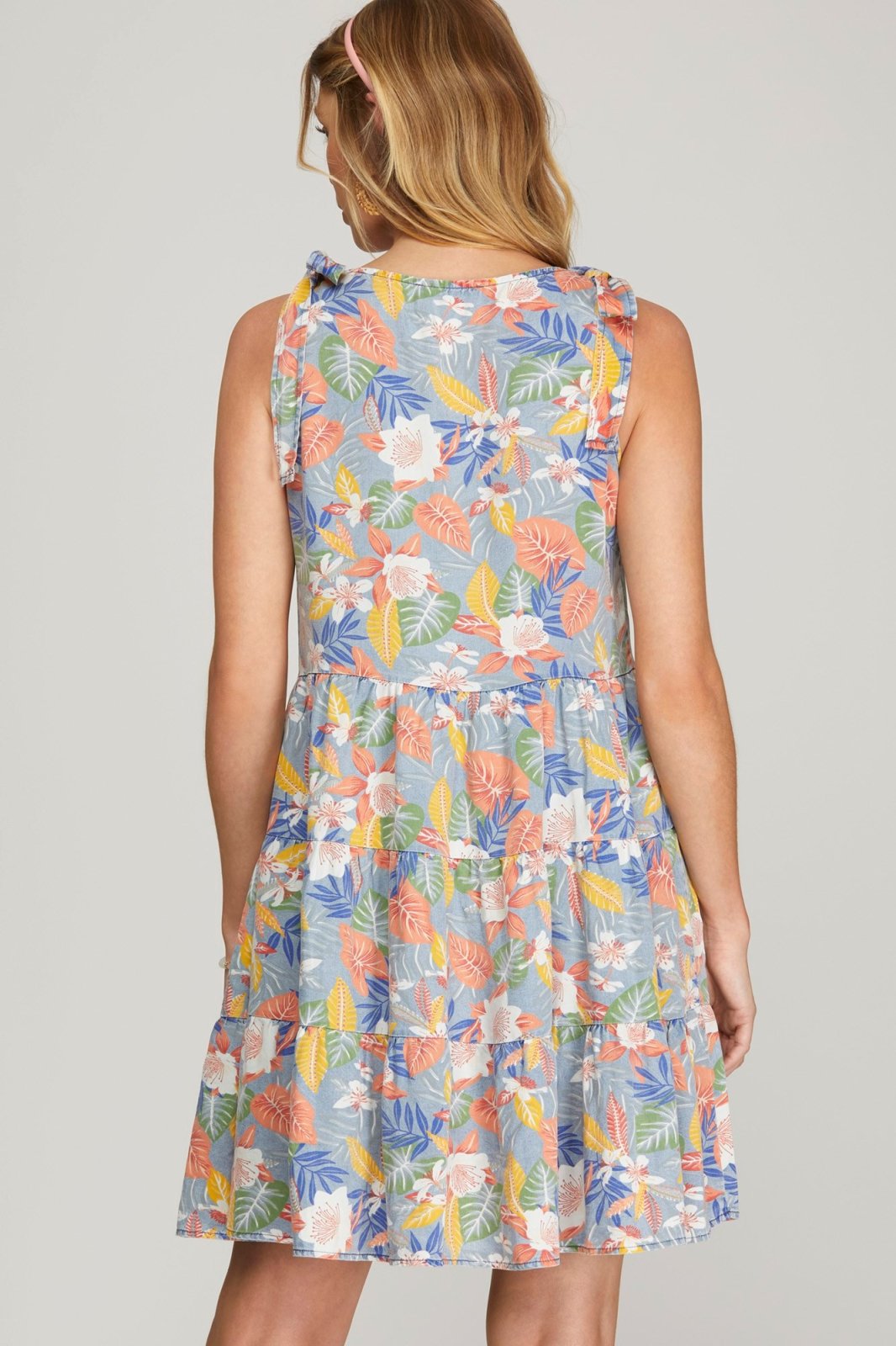 Back view of a woman wearing the SUMMER VIBES DRESS from Raggdoll Boutique, showcasing vibrant floral pattern and trendy coastal style.