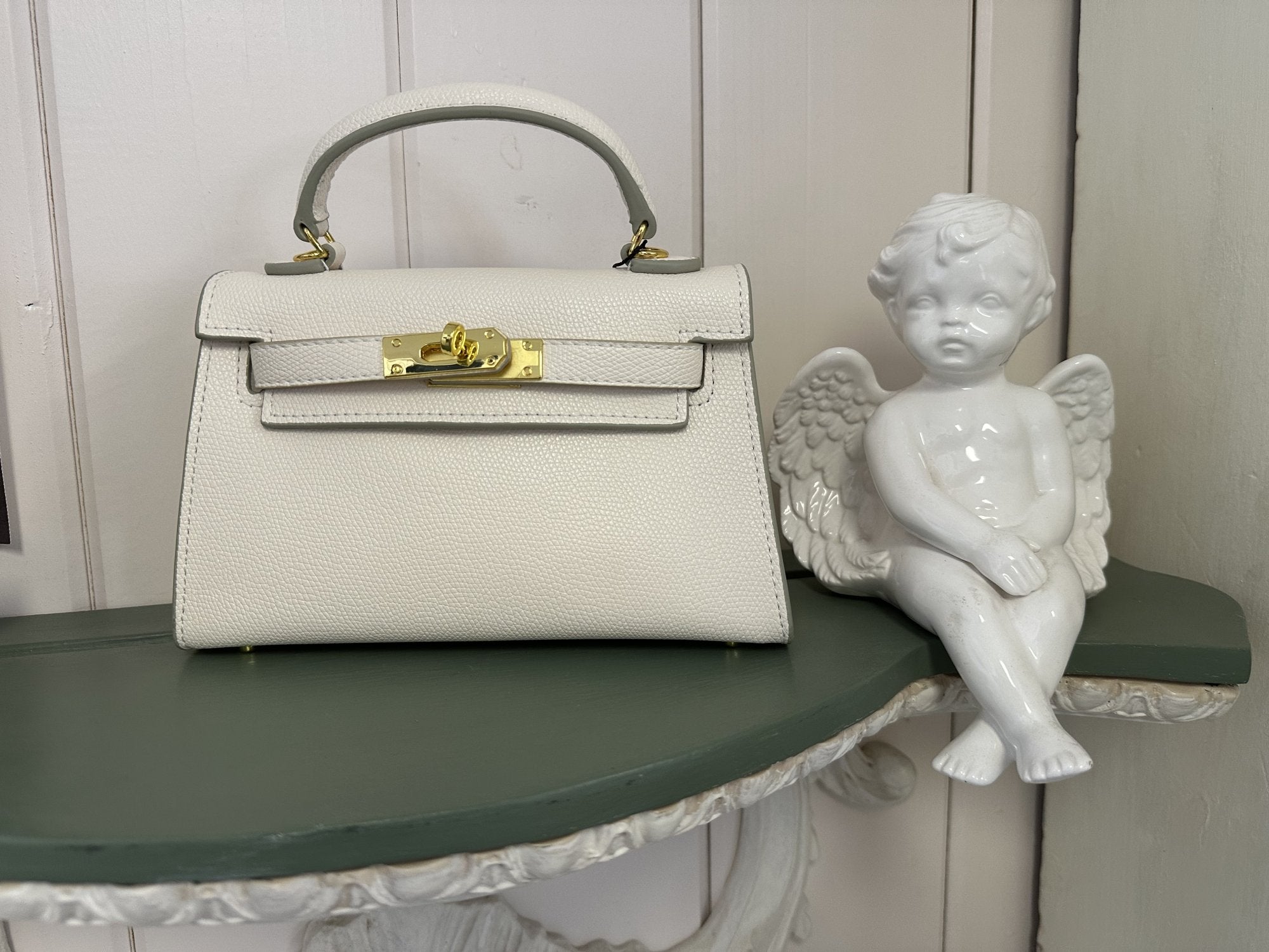 Stylish white Barbara Bag on a green shelf next to a decorative angel figurine, perfect for coastal boutique clothing lovers.