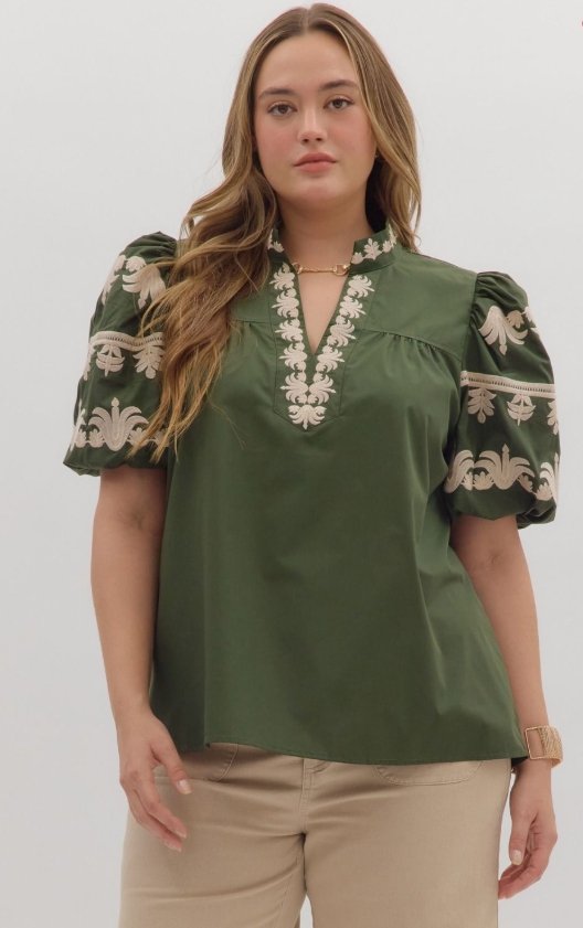 Plus size model wearing the Margot Top, a dark green V-neck pullover with embroidered placket and bubble sleeves.