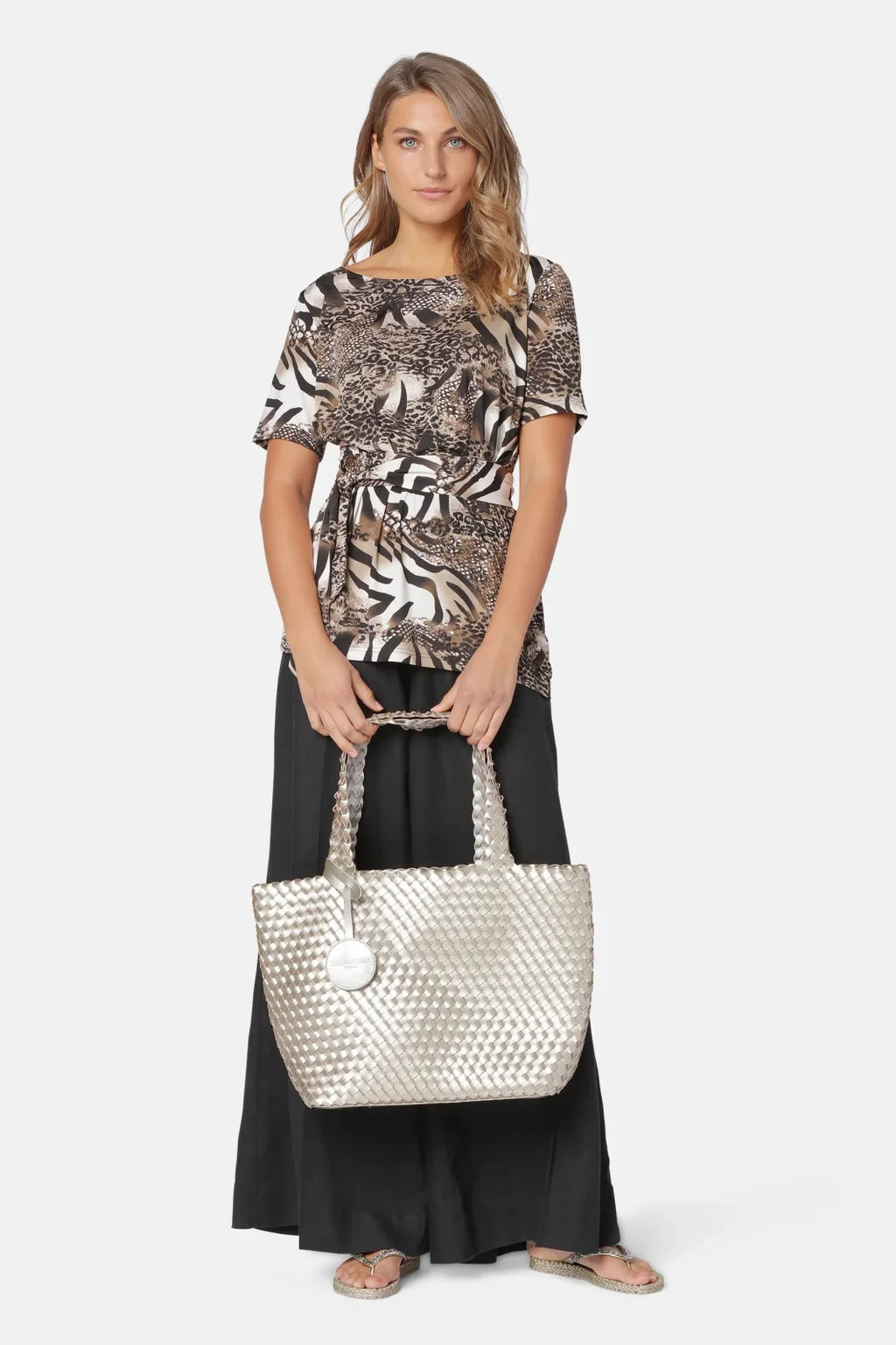 Stylish model in a printed top and black skirt, showcasing the Ilse Jacobsen Platin silver tote bag from a coastal boutique.